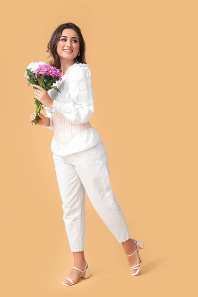 Fashionable woman holding bouquet of flowers and looking aside on color background. International Women's Day - Фото, изображение