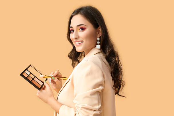 Frau mit kreativem Make-up hält dekorative Kosmetik und Pinsel auf farbigem Hintergrund. Internationaler Frauentag - Foto, Bild
