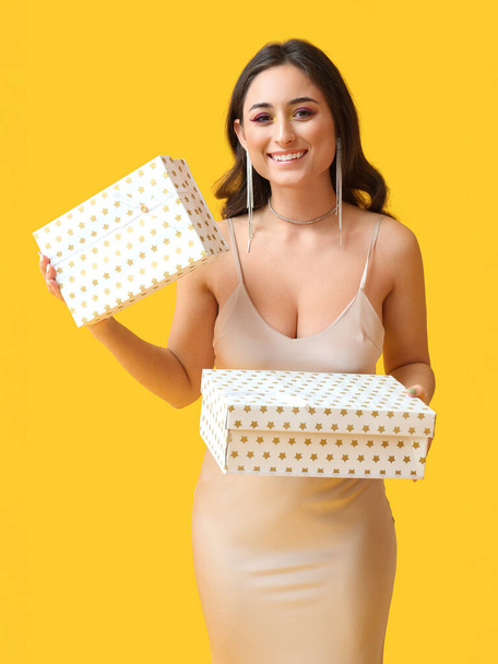 Beautiful woman holding gift boxes on yellow background. International Women's Day - Fotografie, Obrázek