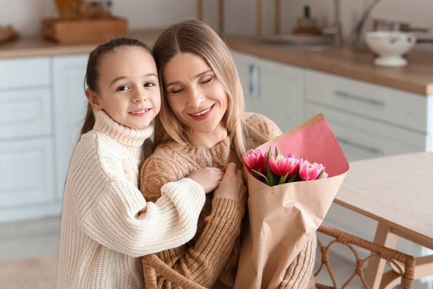 Gelukkige moeder met boeket tulpen en haar dochtertje in de keuken op Internationale Vrouwendag - Foto, afbeelding