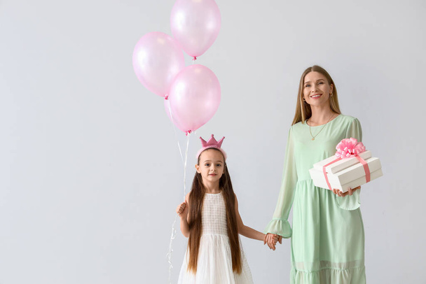 Маленька дівчинка зі своєю матір'ю, подарунком і кулями на світлому тлі. Міжнародний жіночий день - Фото, зображення