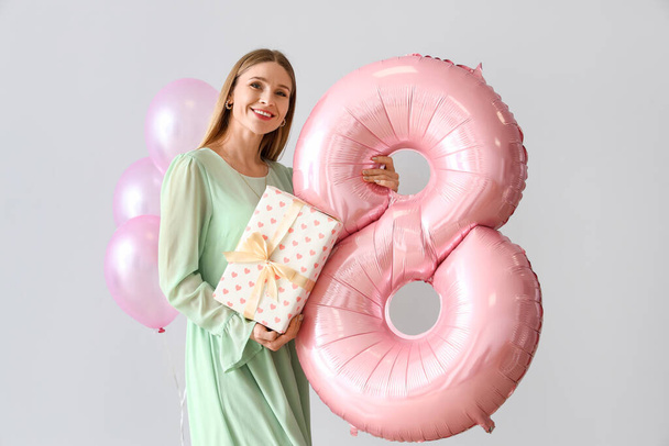 Beautiful woman with gift and balloons on light background. International Women's Day celebration - Foto, immagini