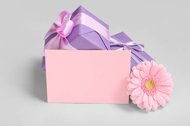 Blank greeting card for International Women's Day, gift boxes and gerbera flower on grey background - Photo, image