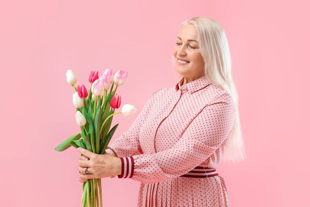 Mooie volwassen vrouw met boeket van tulpen op roze achtergrond, close-up. Internationale Vrouwendag viering - Foto, afbeelding