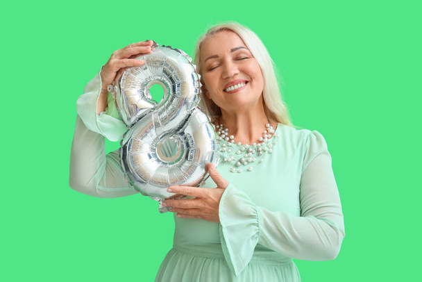 Χαμογελώντας ώριμη γυναίκα με κλειστά μάτια κρατώντας μπαλόνια σε σχήμα του σχήματος 8 σε πράσινο φόντο. Παγκόσμια Ημέρα της Γυναίκας - Φωτογραφία, εικόνα