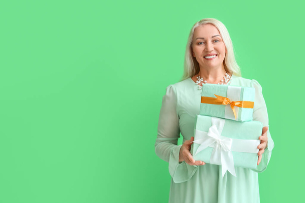 Módní zralá žena drží hromadu dárkových krabic na zeleném pozadí. Mezinárodní oslava Dne žen - Fotografie, Obrázek