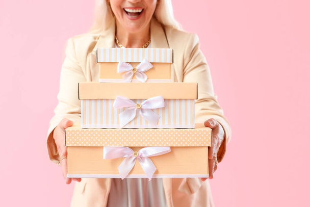 Hymyilevä kypsä nainen, jolla on pino lahjapakkauksia vaaleanpunaisella taustalla, lähikuva. Kansainvälinen naistenpäivä juhla - Valokuva, kuva