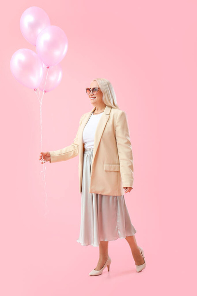 Mature woman holding air balloons on pink background. International Women's Day celebration - Zdjęcie, obraz