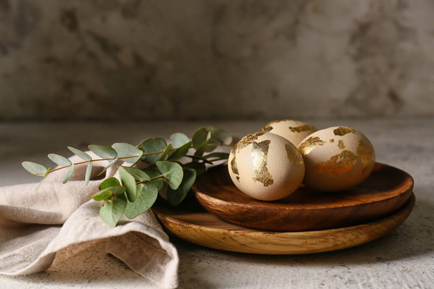 Деревянные тарелки с красивыми пасхальными яйцами и эвкалиптовыми ветвями на светлом фоне - Фото, изображение