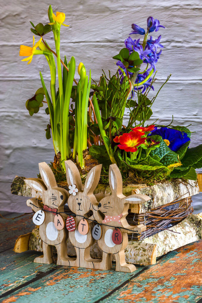 Квіткова композиція з дерев'яними великодніми кроликами як прикраса і текст Великодня на великодні яйця
. - Фото, зображення