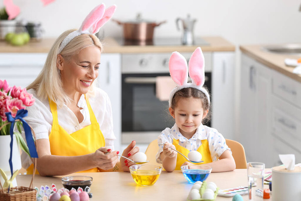 Το κοριτσάκι και η γιαγιά της βάφουν πασχαλινά αυγά στο σπίτι. - Φωτογραφία, εικόνα
