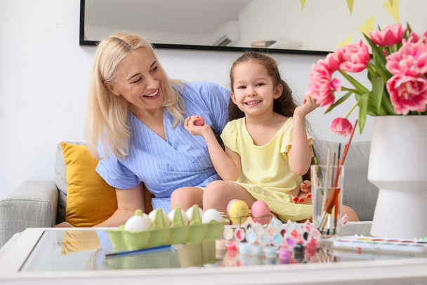 Petite fille et sa grand-mère peignant des œufs de Pâques à la maison - Photo, image