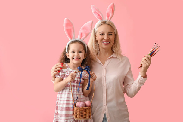 Joyeux petite fille et sa grand-mère avec des œufs de Pâques dans le panier et brosses sur fond de couleur - Photo, image