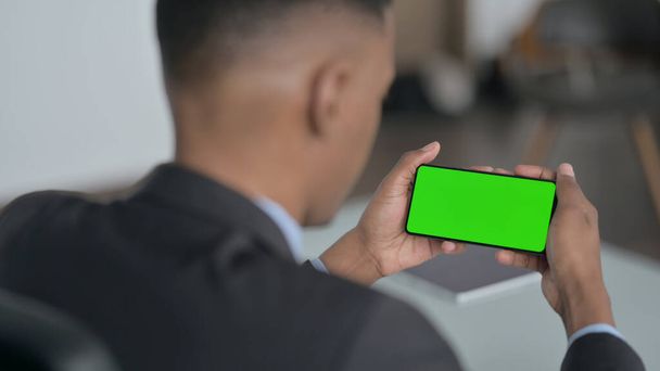 Vista trasera del empresario africano que mira el teléfono inteligente con pantalla de croma - Foto, Imagen