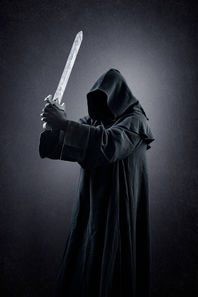 Warrior with hooded cape and medieval sword over dark misty background - Fotó, kép