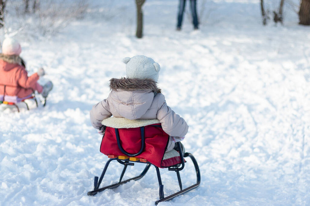 Małe dziecko w ciepłych ubraniach i kapelusz zsuwa się ze wzgórza na sankach po śniegu. - Zdjęcie, obraz