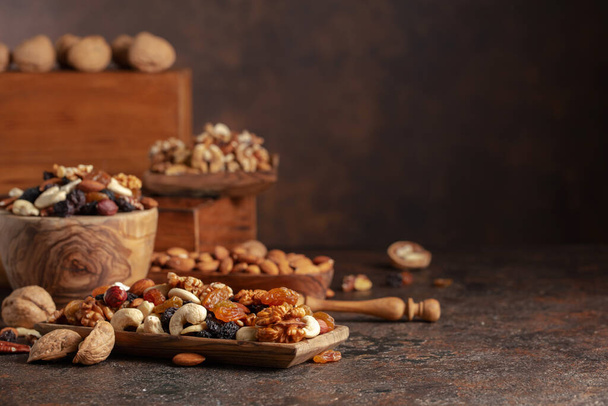 Meng van noten en rozijnen op een bruine rustieke achtergrond. Gepresenteerde rozijnen, walnoten, hazelnoten, cashewnoten, pecannoten en amandelen. - Foto, afbeelding