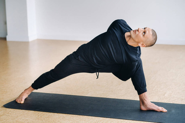 Muž v černém sportovní oblečení dělá jógu, protahuje se v tělocvičně. - Fotografie, Obrázek