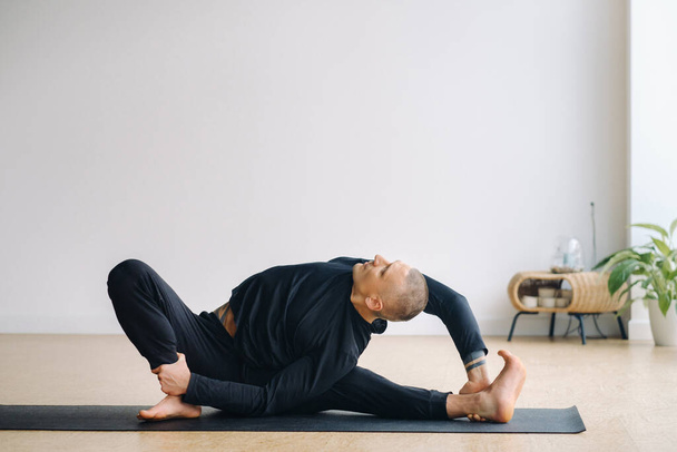 A man in black sportswear is doing Yoga, stretching in the gym. - Фото, изображение