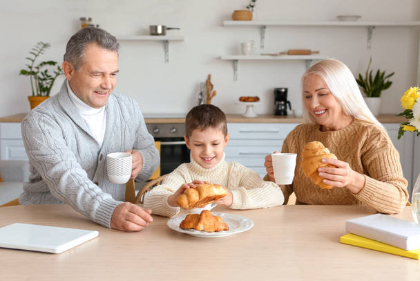 Kleiner Junge und seine Großeltern mit Tassen Kakao und Croissants zu Hause - Foto, Bild