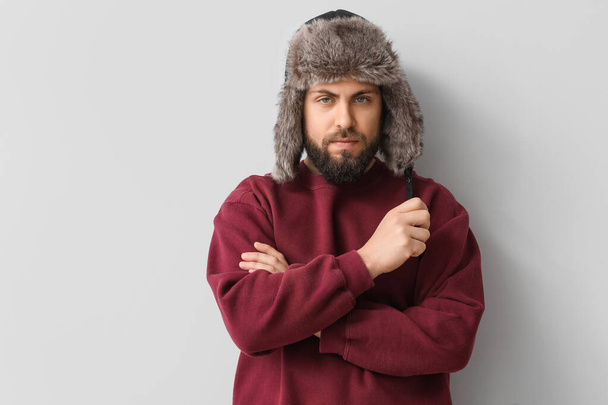 Stylish bearded man in sweater and ear-flapped hat on light background - Photo, Image
