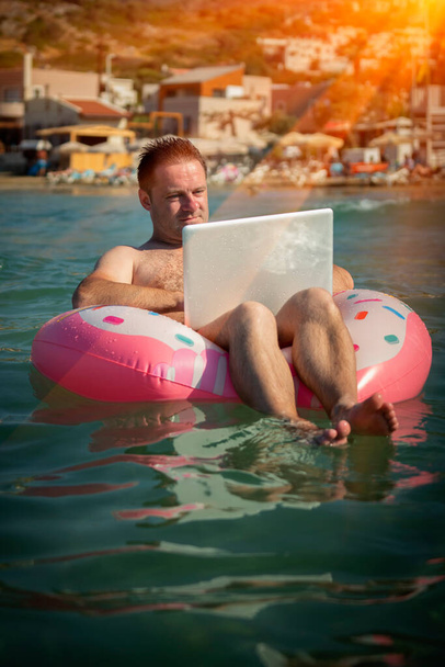 Trabajando siempre y en todas partes. Retrato humorístico del freelancer masculino trabajando con laptop al aire libre en agua de mar tropical. - Foto, imagen