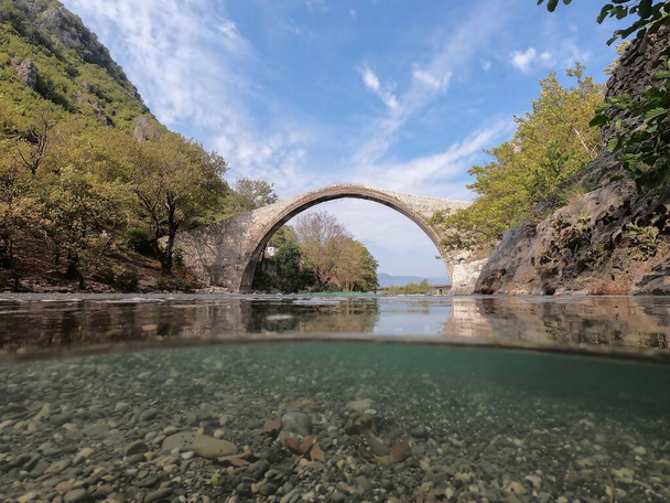 コニツァ、アオス川、半分水中ビュー、エピルス、ギリシャの古い石造りの橋 - 写真・画像