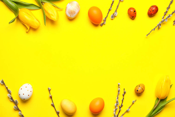 Beautiful Easter eggs, willow branches and tulip flowers on yellow background - Photo, Image