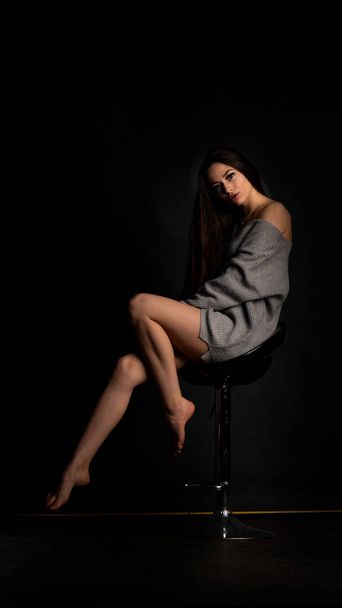 mooi sexy meisje, poseren een korte grijze jurk, zwarte achtergrond stoel - Foto, afbeelding