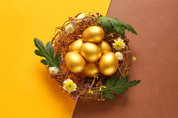 Гнездо с золотыми окрашенными пасхальными яйцами и цветами на фоне цвета - Фото, изображение
