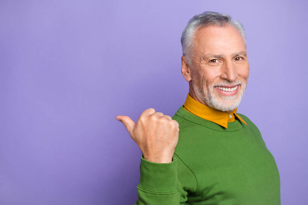 Foto de hombre positivo pensionista vestido jersey verde apuntando hacia atrás espacio vacío aislado color púrpura fondo. - Foto, imagen