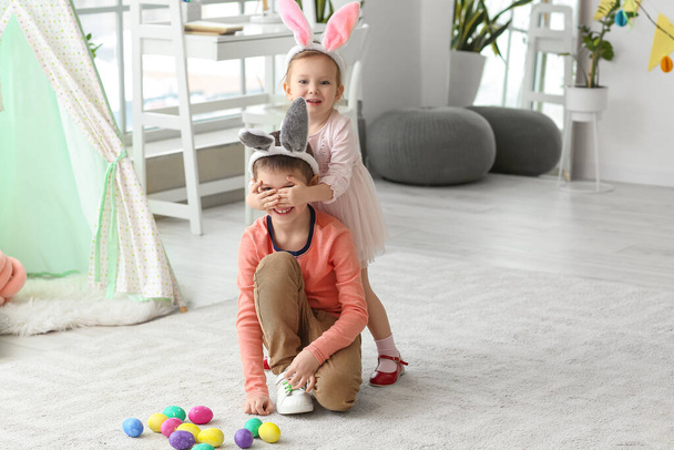 Cute little girl in bunny ears closing her brother's eyes at home on Easter day - Fotografie, Obrázek