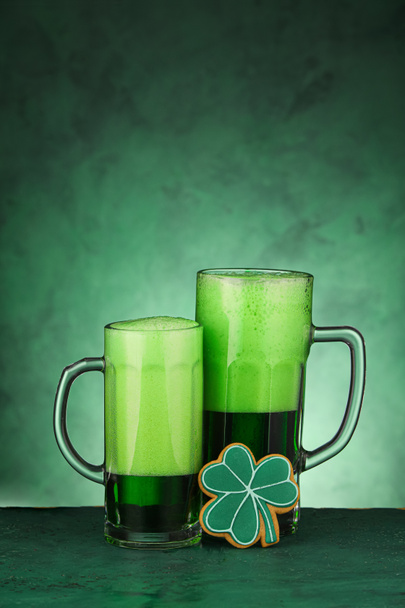 Vasos de cerveza y galletas de jengibre para la celebración del Día de San Patricio sobre fondo verde - Foto, imagen