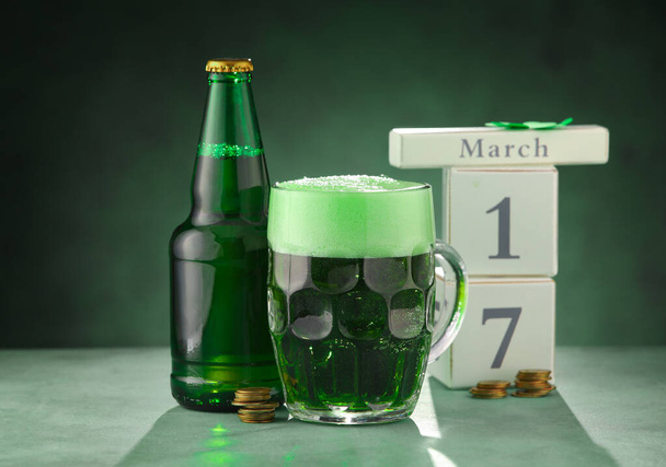 緑の背景にカレンダー付きのビールのグラスとボトル。聖パトリックの日のお祝い - 写真・画像