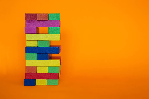Houten toren spel blokken geïsoleerd op oranje achtergrond met kopieerruimte. Kleurrijke toren gemaakt van houten blokken. - Foto, afbeelding