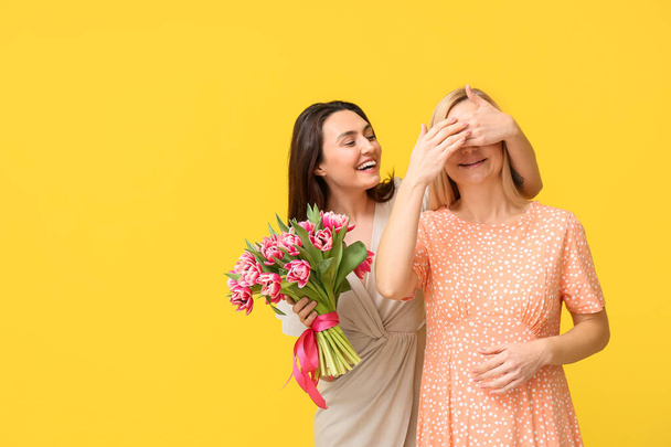 Beautiful woman with bouquet of flowers greeting her friend on color background. International Women's Day celebration - Foto, Imagem
