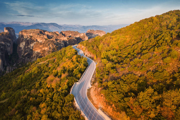 ギリシャのメテオラ修道院近くの鬱蒼とした森の間の風光明媚な蛇紋岩の道路上の空中トップビュー - 写真・画像