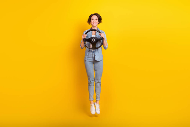 Full length photo of young woman jump up energetic hold steerimg-wheel vacation isolated over yellow color background - Fotó, kép