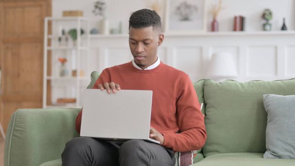 アフリカの男はソファを残し、ノートパソコンを閉じる - 写真・画像