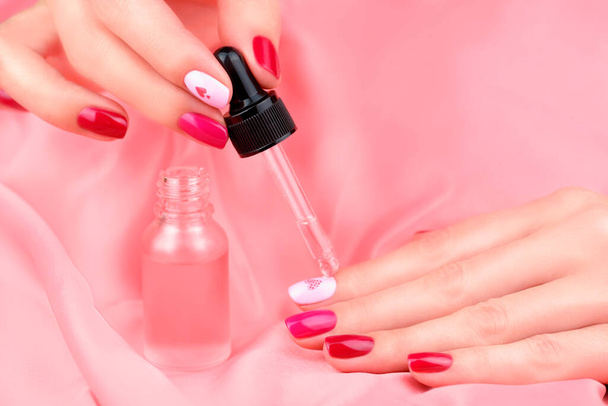 Women's hands with a beautiful manicure in different pink colors. Manicure and cuticle care. A woman's hand drips care oil from a bottle onto her nails. Close up - Fotó, kép