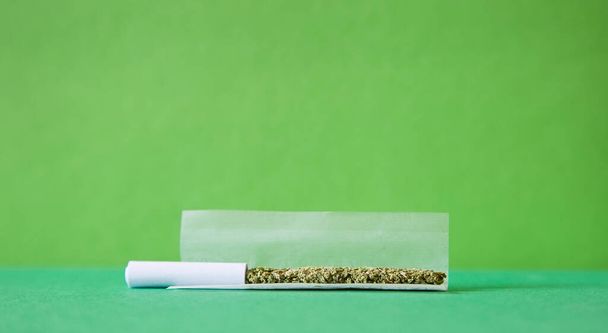 marijuana in rolling cigarette, mouthpiece, paper, green background - Photo, image