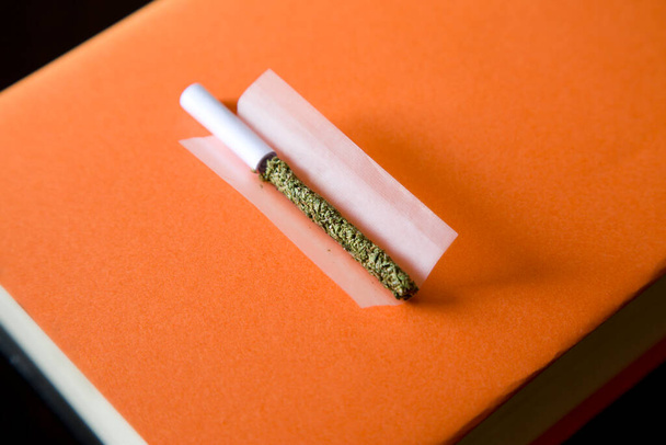 marijuana dans la cigarette roulante, embout buccal, papier, fond de livre orange. - Photo, image