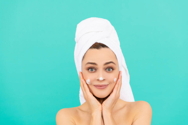alegre joven aplicación de crema facial sobre fondo azul - Foto, Imagen