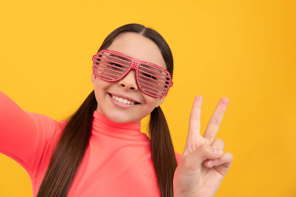 vrolijk kind maken selfie in glamour party bril op gele achtergrond, vrede - Foto, afbeelding