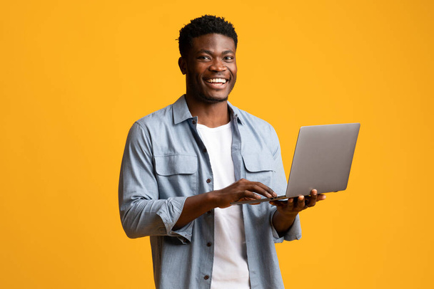 Handsome black man using modern laptop on yellow - Foto, afbeelding