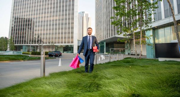 entrepreneur in businesslike suit holding shopping bag and giftbox outside the office, business. - Photo, Image