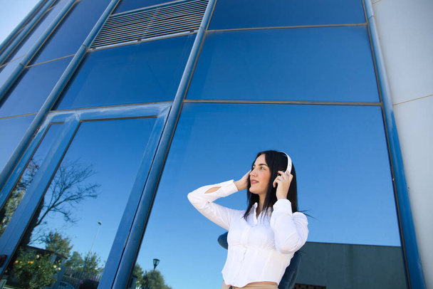Mujer escuchando música y divirtiéndose - aislada sobre el fondo de cristal de un edificio de oficinas. Concepto de música y entretenimiento. - Foto, imagen