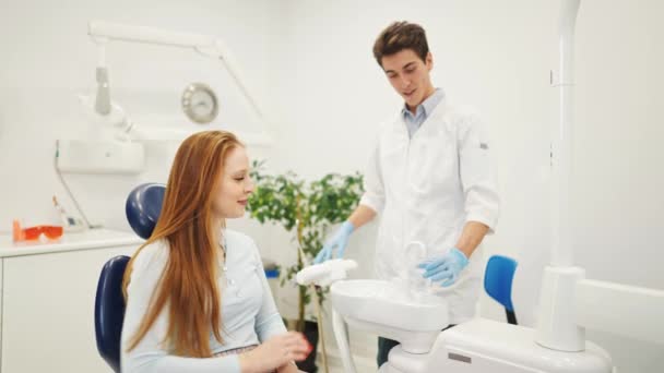 Paciente femenina joven en silla dental que enjuaga la boca con agua antes durante la cita con el dentista - Imágenes, Vídeo