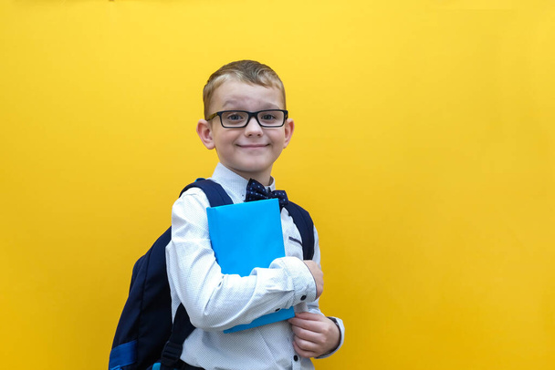 A happy boy in glasses and a school backpack holds a book in his hands. - Φωτογραφία, εικόνα
