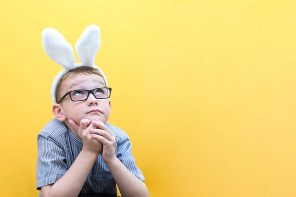 A happy boy with glasses has put on rabbit ears and is dreaming . easter is coming soon - Фото, зображення